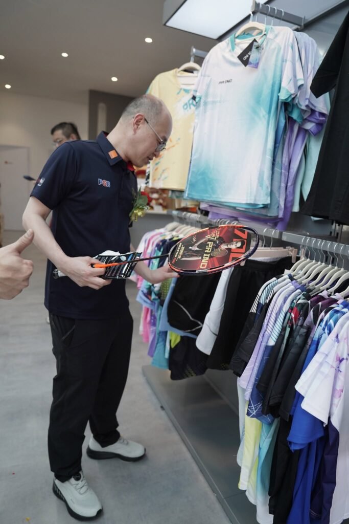 A customer looking at a racket beside the PRIND apparel rack